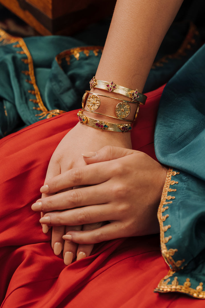 woman wearing a 18k gold-plated fish and floral stacked bangle bracelet set.