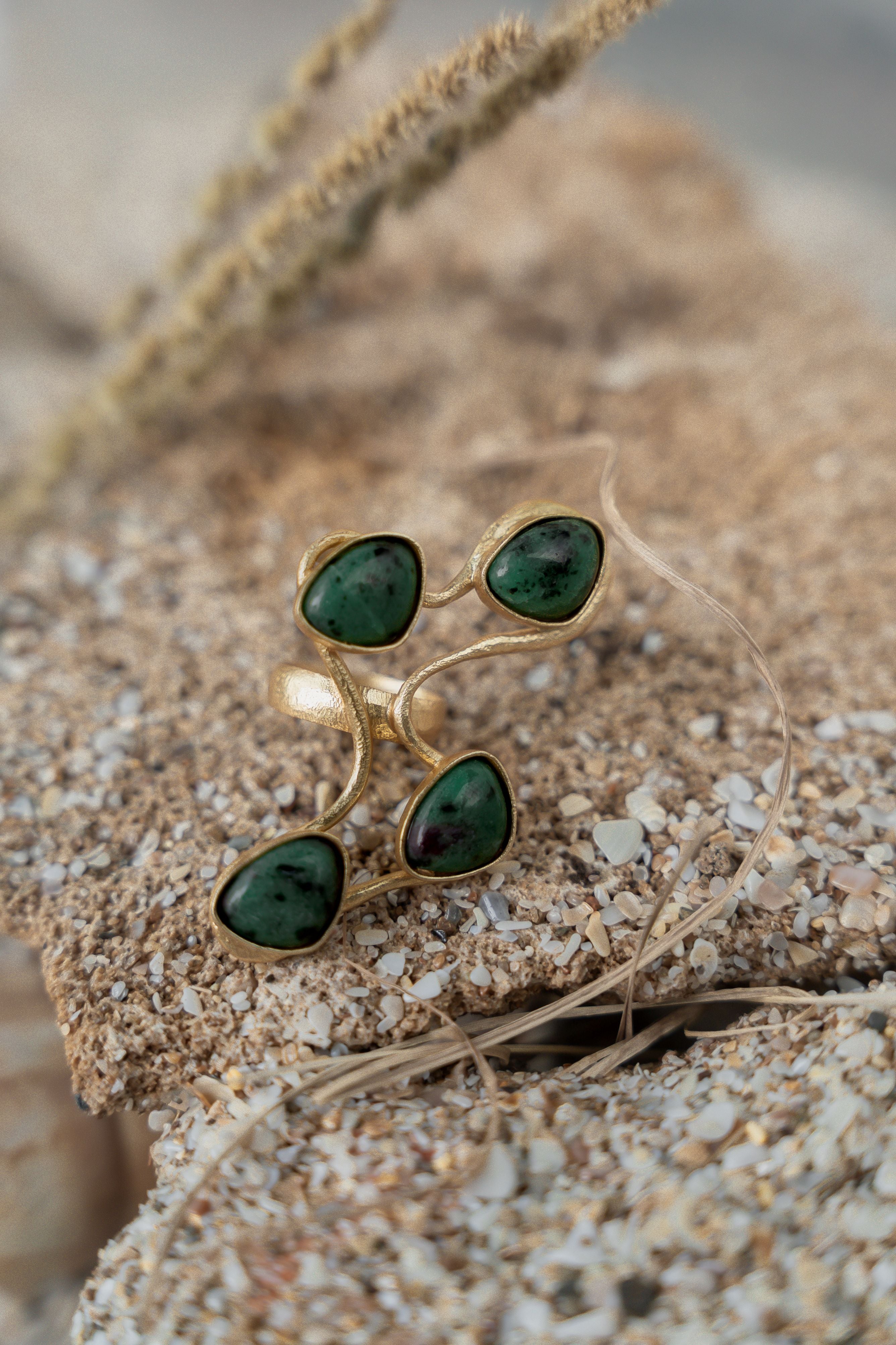 A gold-colored ring with green gemstones placed on a sandy surface.