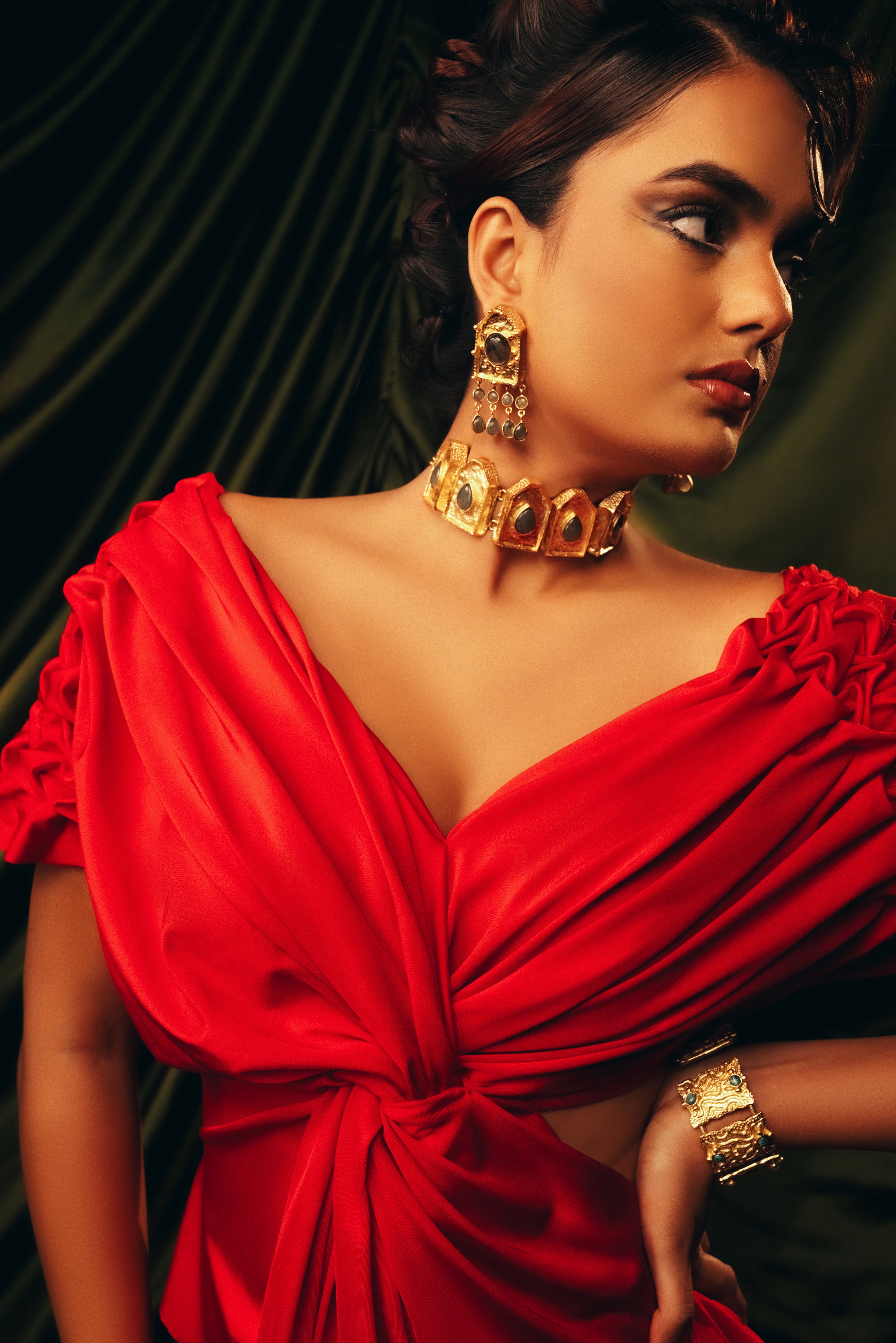 Close-up of a woman wearing a statement gold choker necklace featuring black or dark stone embellishments and red attire.