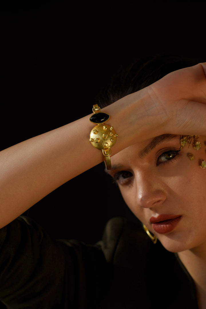 Gold cuff lock bracelet with black onyx gemstone worn on a woman's wrist