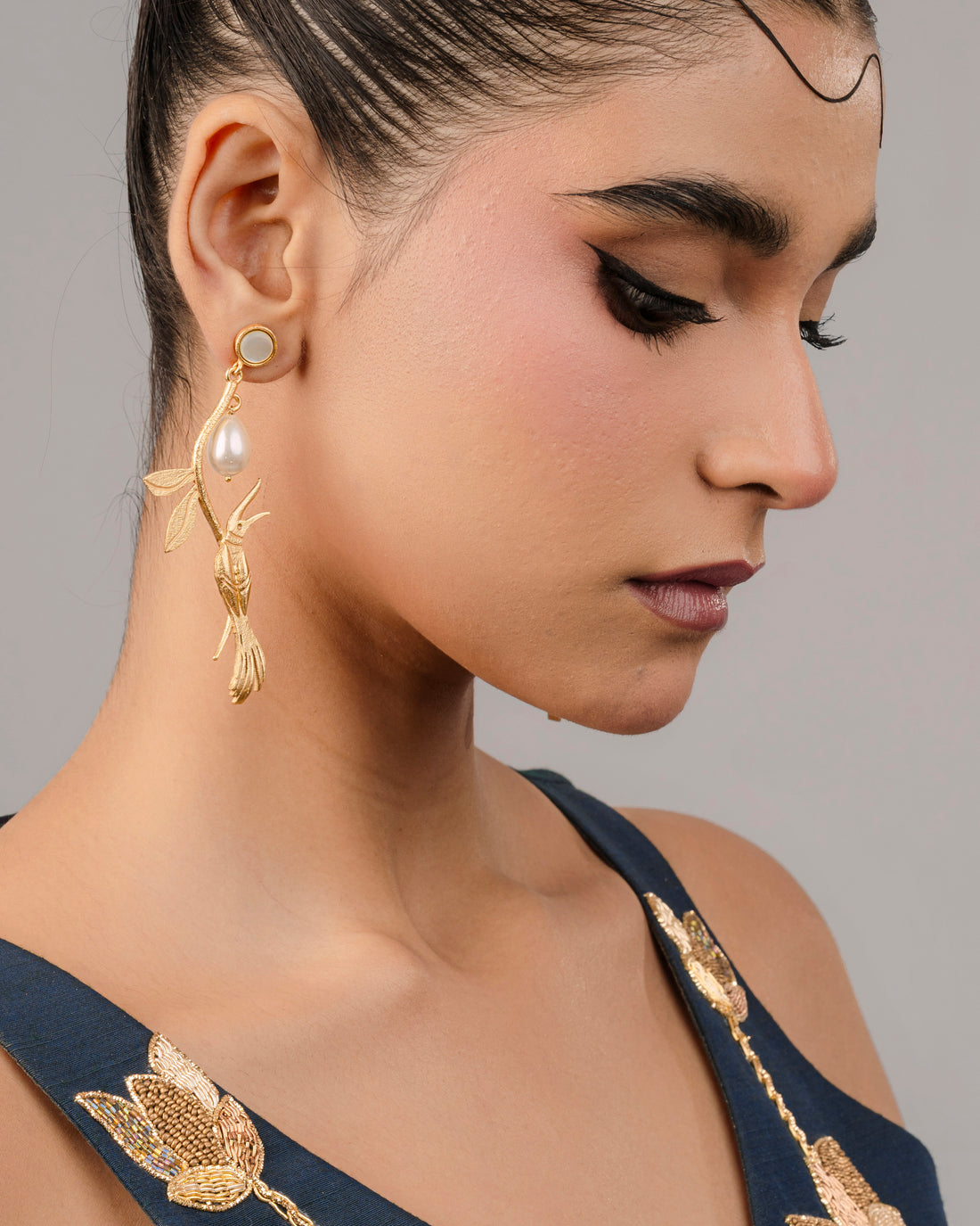 dramatic gold-plated statement earring featuring an intricate textured twig-and-leaf design and a dangling teardrop pearl.