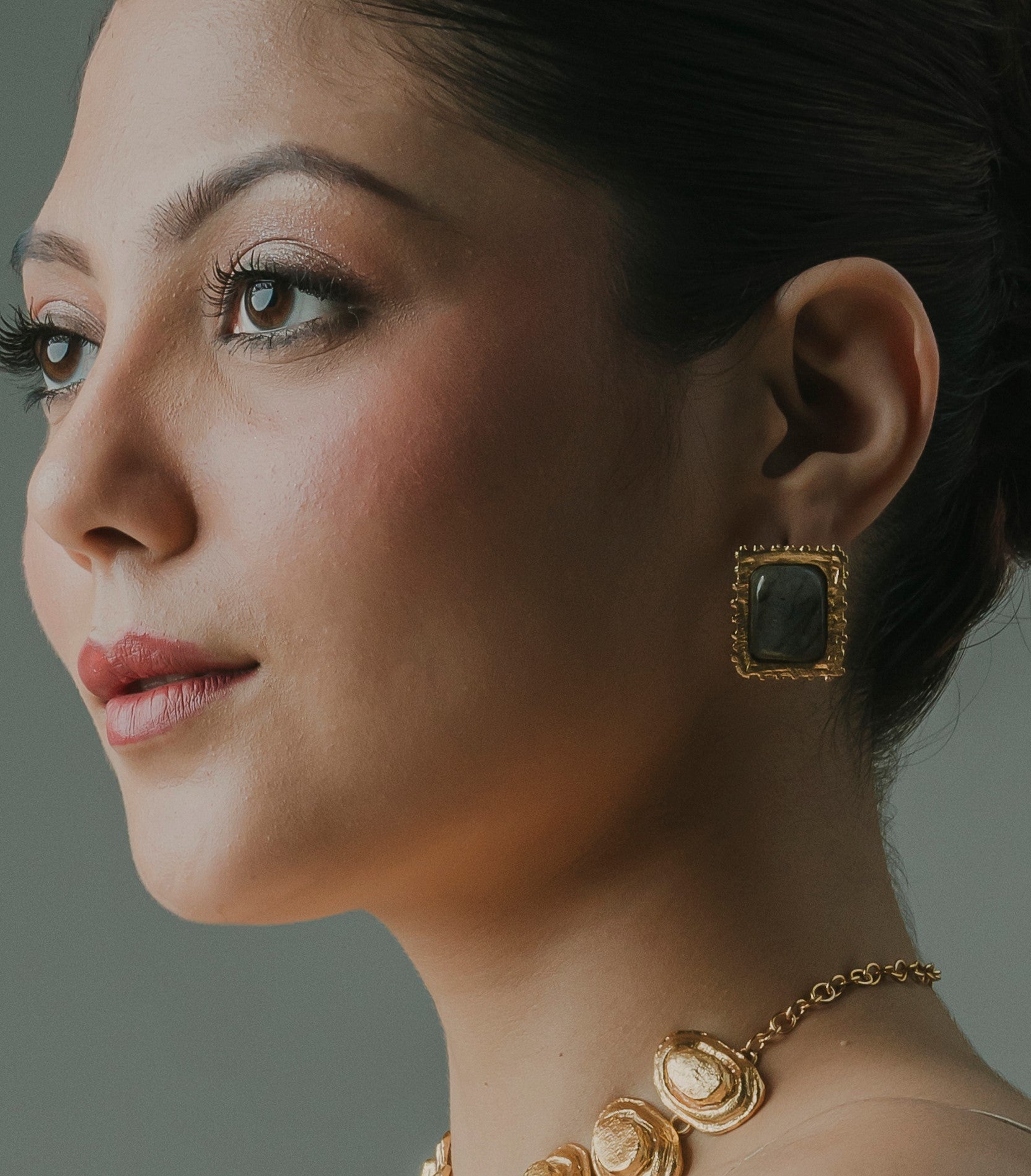 Woman wearing Lebra 18k gold-plated rectangular stud earrings with a grey central stone by Baalajewels.