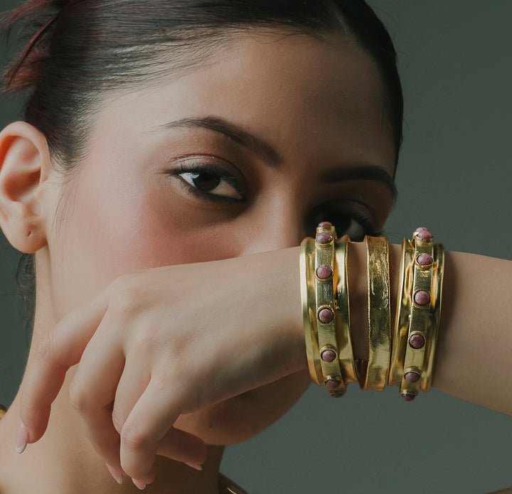Set of 3 gold stackable kada bracelets with pink rose quartz stones worn on a woman's wrist
