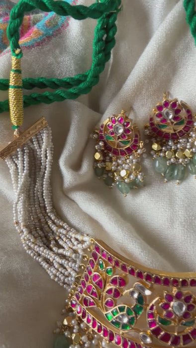 A premium gold-plated imitation jewelry set showcasing a traditional crescent-shaped choker with multi-strand pearl bands and matching ethnic dangle earrings detailed with fine Kundan work and green polished beads.
