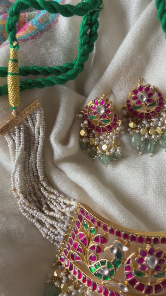 A premium gold-plated imitation jewelry set showcasing a traditional crescent-shaped choker with multi-strand pearl bands and matching ethnic dangle earrings detailed with fine Kundan work and green polished beads.