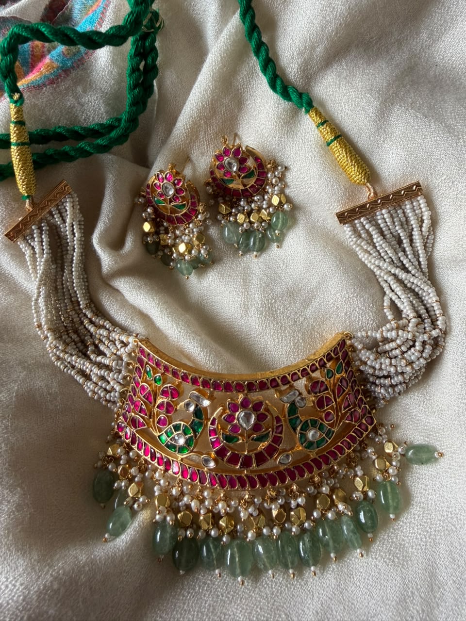 Traditional Indian heritage jewelry set including a wide gold-toned choker necklace and drop earrings adorned with intricate pink and green enameling, classic Kundan setting, and a border of cascading green gemstone drops.