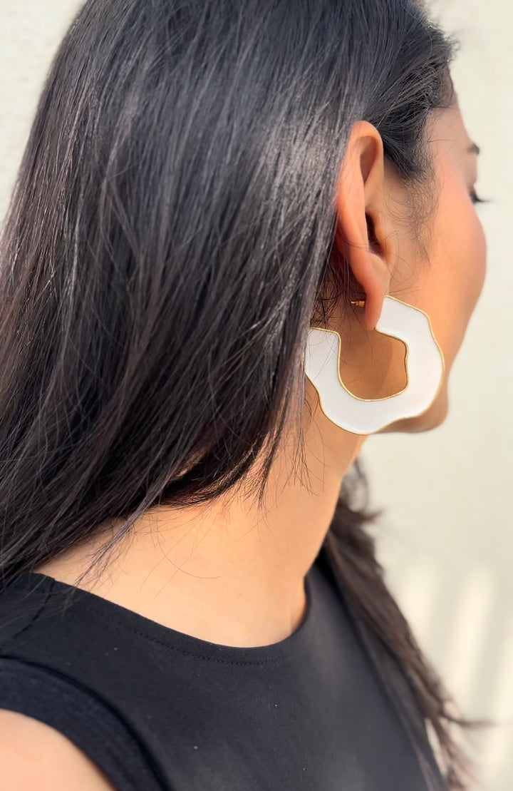 White chunky wave hoop earrings with 18k gold-toned plating worn by a model.